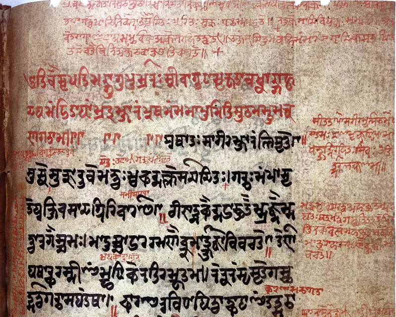 Page d’un manuscrit sanskrit : lignes de dévanagari à l’encre noire, gloses et titres à l’encre rouge dans la marge et entre les lignes.